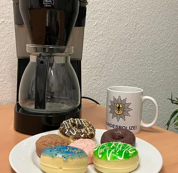Kaffeemaschine, Donuts und Bundespolizei-Tasse auf Tisch.