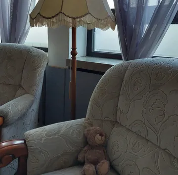 Teddybär auf Sessel neben Lampe und Vorhang.