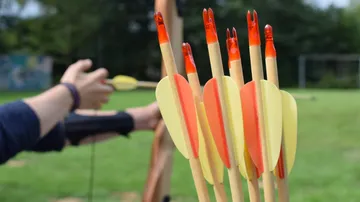 Arrows in holder, person drawing bow outdoors.