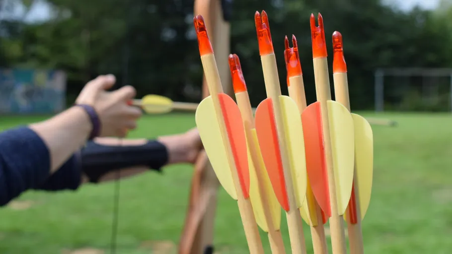 Arrows in holder, person drawing bow outdoors.