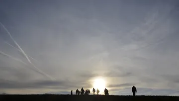 Silhouetted people walking at sunrise on a hill.
