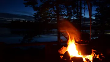 Topf über Lagerfeuer am See während Sonnenuntergang.