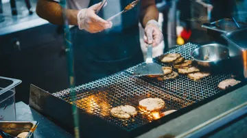 Chef grilling meat on a barbecue grill.