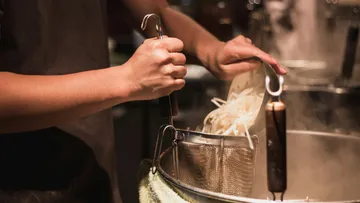 Person cooking with a wire mesh basket.