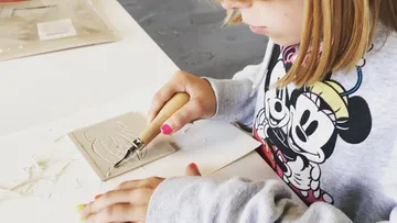 Child carving design into clay slab indoors.