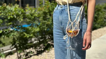Person trägt Weinglas in Makramee-Halter im Freien.
