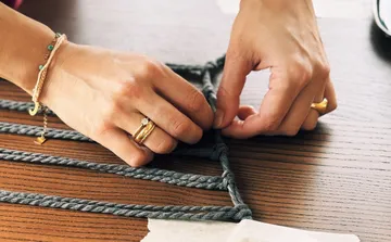 Hände binden graues Seil auf Holztisch.