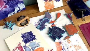 Colorful prints and carving tools on wooden table.