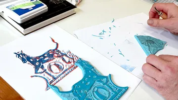 Person carving a blue linocut print.