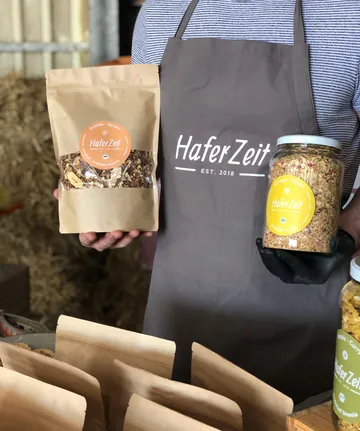 Person hält HaferZeit-Granola-Produkte drinnen.