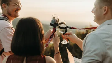 Menschen stoßen draußen bei Sonnenuntergang mit Weingläsern an.