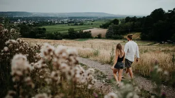 Couple walking on path through grassy landscape.