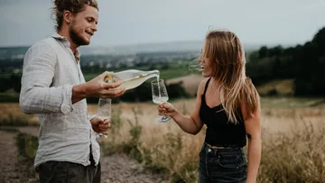 Man pours drink for woman in vineyard.