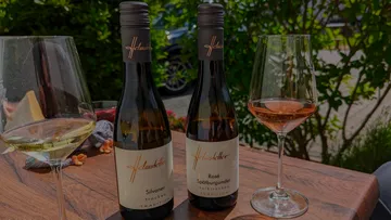 Two wine bottles and glasses on table outdoors.