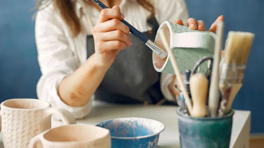 Person painting pottery with a brush indoors.