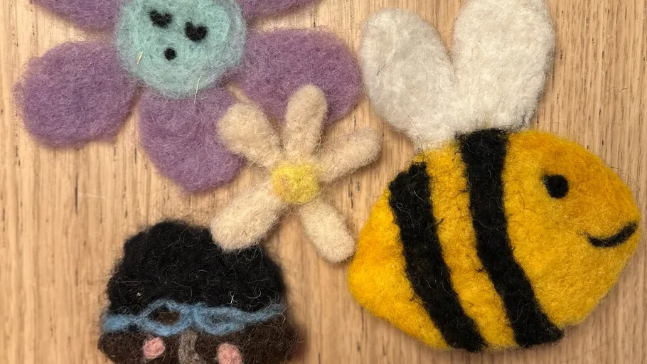 Felt bee and flowers on wooden surface.