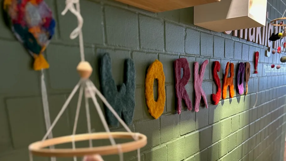 Bunte Filzbuchstaben "WORKSHOP" an Ziegelwand.