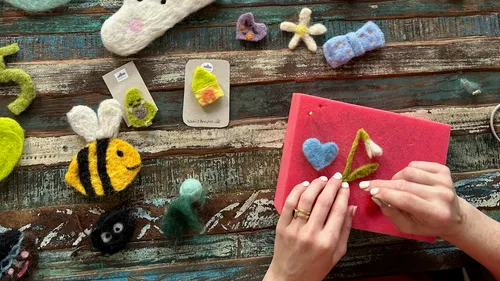 Hände filzen bunte Wollformen auf Tisch.