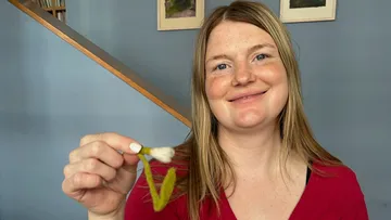 Person smiling, holding a plant indoors.