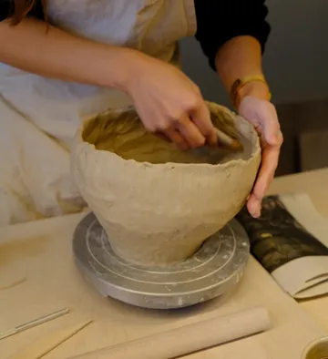 Person shaping clay bowl on pottery wheel.