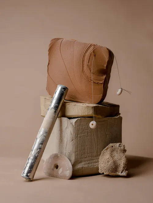 Abstrakte Tonskulptur mit Metallrohr vor braunem Hintergrund.