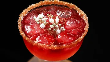 Red cocktail with ice and flower garnish.