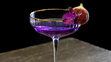 Lila Cocktail mit Feige und Blume garniert.