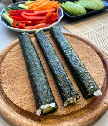 Sushi rolls on wooden plate, vegetables nearby.