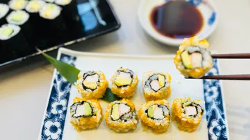Sushi-Rollen auf einem Dekoteller, Stäbchen halten eine.