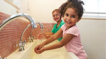 Children washing hands at a sink, smiling.