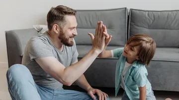 Mann und Junge geben High-Five im Wohnzimmer.