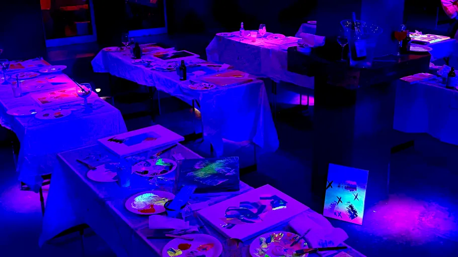 Paint party tables illuminated under black lights.