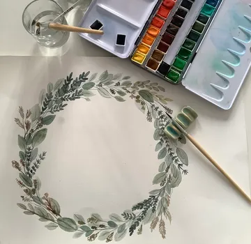 Watercolor wreath painting with brushes and palette.