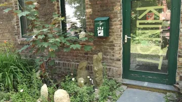Green door labeled 'KUNST,' brick wall, garden.
