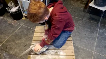 Child carving stone indoors on wooden board.