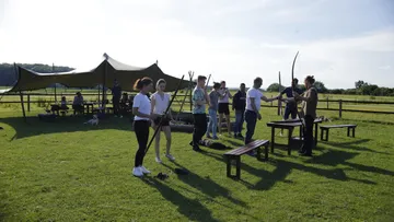 Group practicing archery on a sunny field.