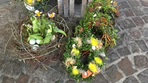 Wreaths and nest with plants on cobblestone ground.