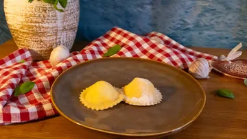 Two ravioli on a brown plate, rustic setting.