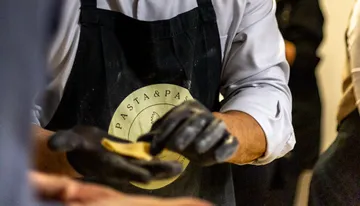 Person folding dough wearing a "Pasta & Pasta" apron.