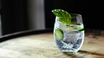 Glass with water, cucumber, basil on barrel.