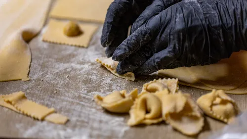 Hands folding fresh pasta dough on floured surface.