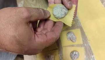 Person preparing ravioli with filling in kitchen.