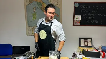Mann in Schürze bereitet Essen in Küche zu.