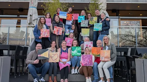 Group of people holding colorful paintings outside.