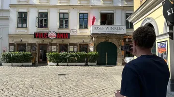 Man photographing historic building on cobblestone street.