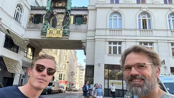 Zwei Männer posieren vor einer historischen Uhr.
