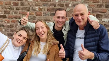 Vier Leute lächeln, Daumen hoch, Ziegelwand.