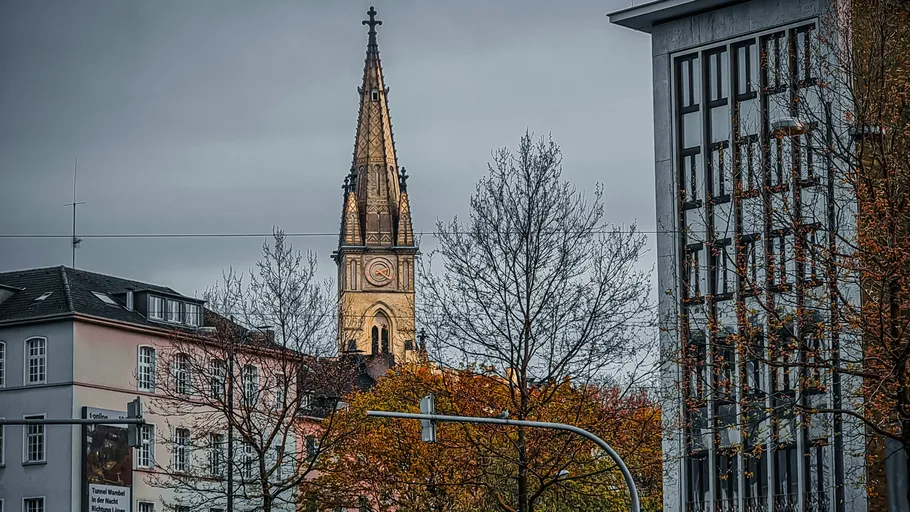 Church tower behind city buildings, bare trees.