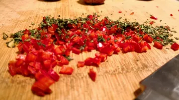 Chopped red pepper and herbs on cutting board.