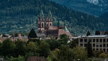 Gothic church towers in a wooded mountainous setting.